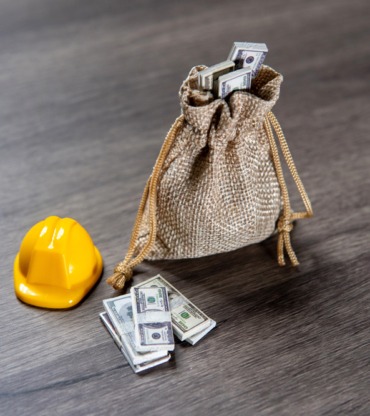 WEBcloseup-image-a-bag-of-money-and-a-hard-hat-on-a-w-2025-03-15-22-03-17-utc